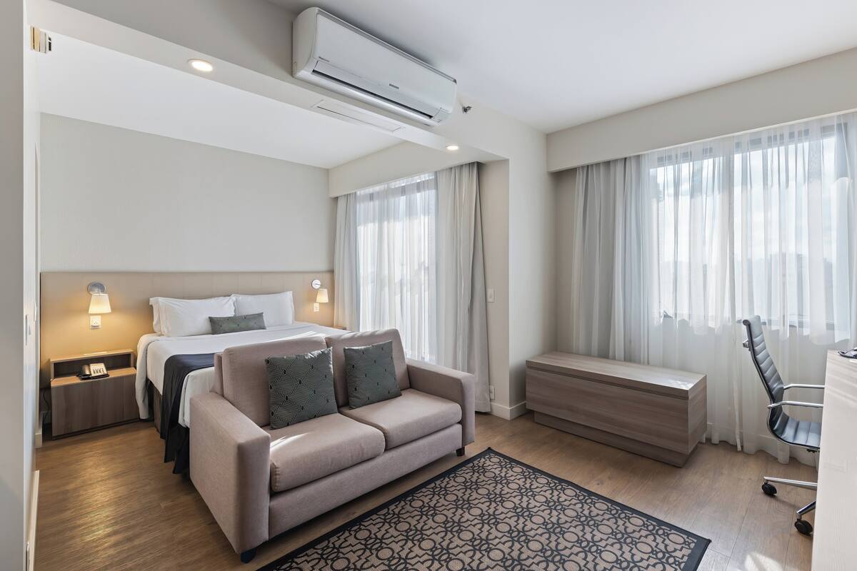 Une chambre d’hôtel moderne équipée d’un lit, d’un canapé, d’un bureau et d’un appareil de climatisation.