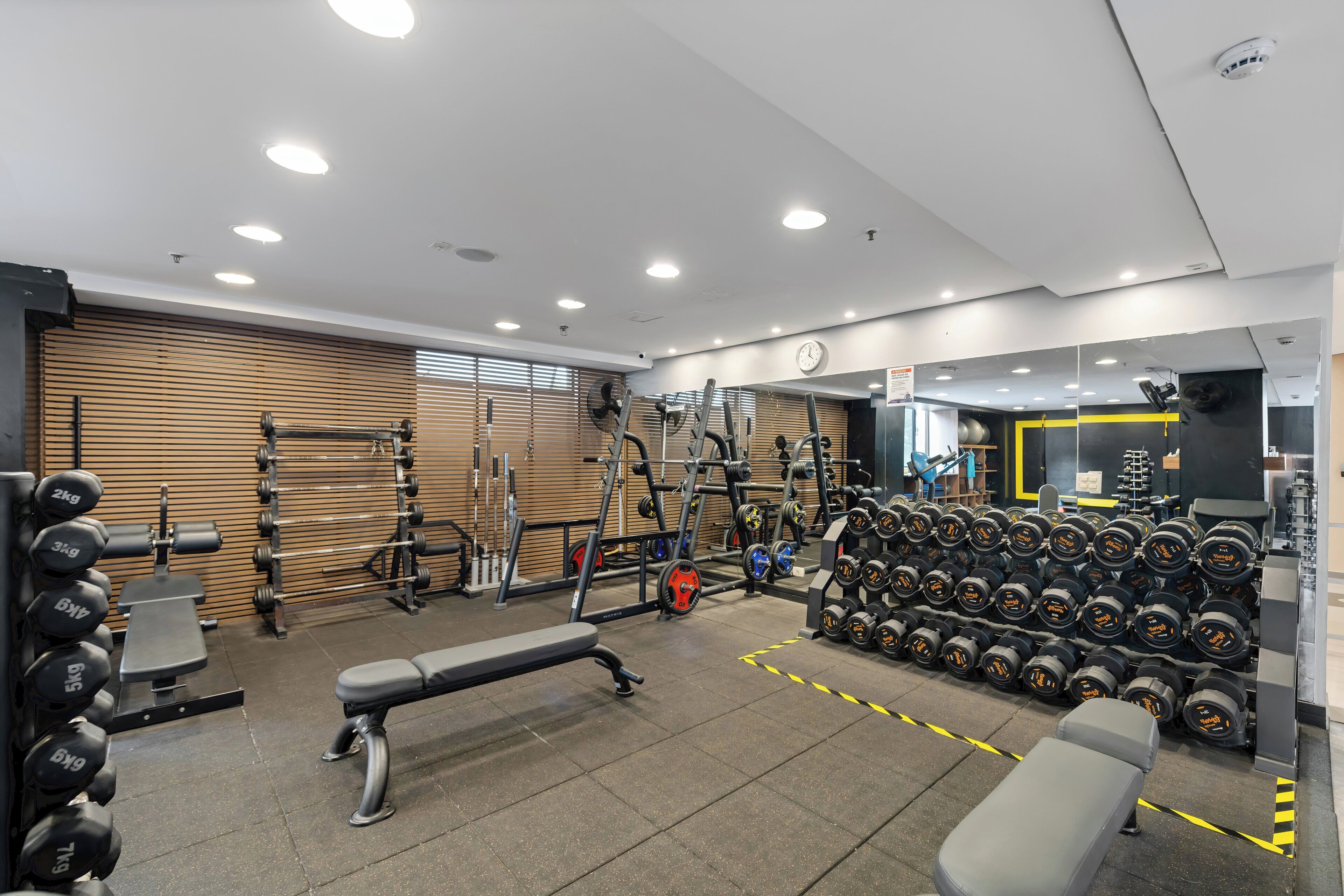 A gym with weightlifting equipment, benches, and a mirrored wall.
