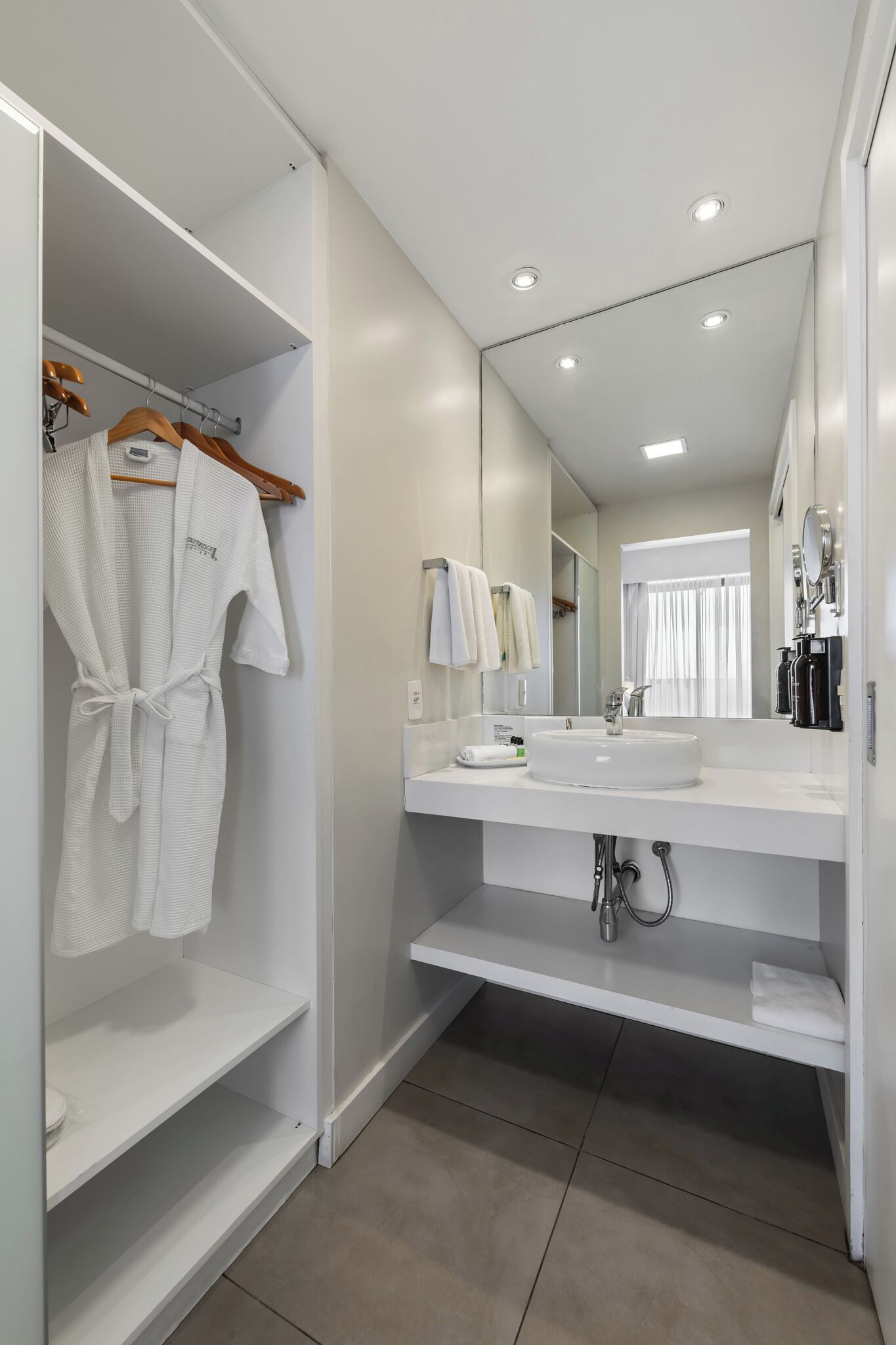 A modern bathroom with a white vanity, a large mirror, and a robe hanging on a rack.