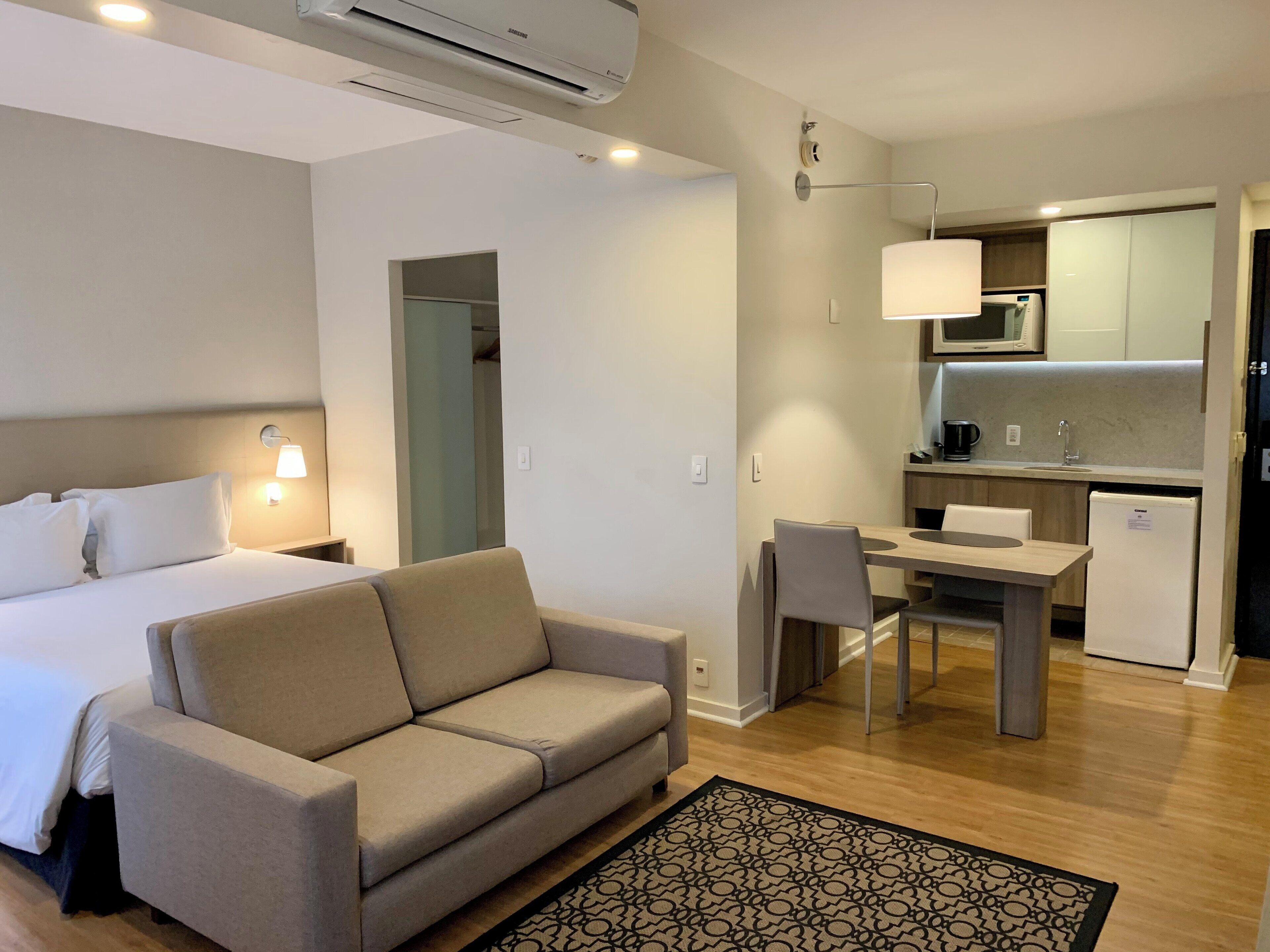 A hotel room with a bed, a sofa, a desk, and a kitchenette.