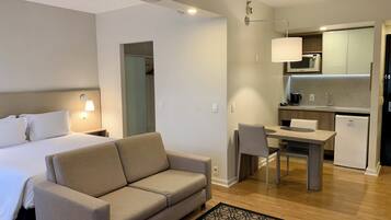 A hotel room with a bed, a sofa, a desk, and a kitchenette.