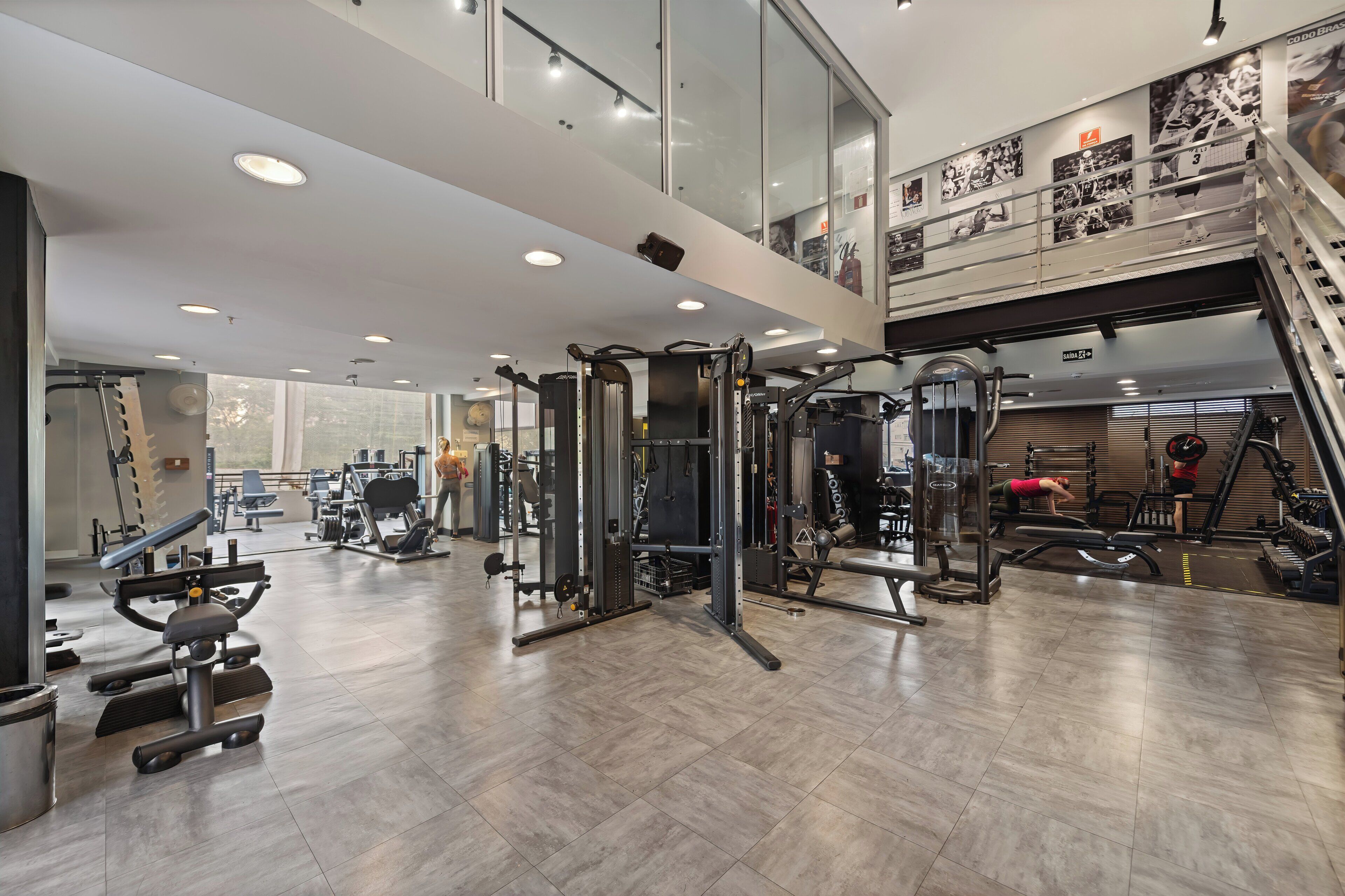 A spacious gym with various exercise equipment, a mezzanine level, and a staircase.