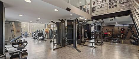 A spacious gym with various exercise equipment, a mezzanine level, and a staircase.