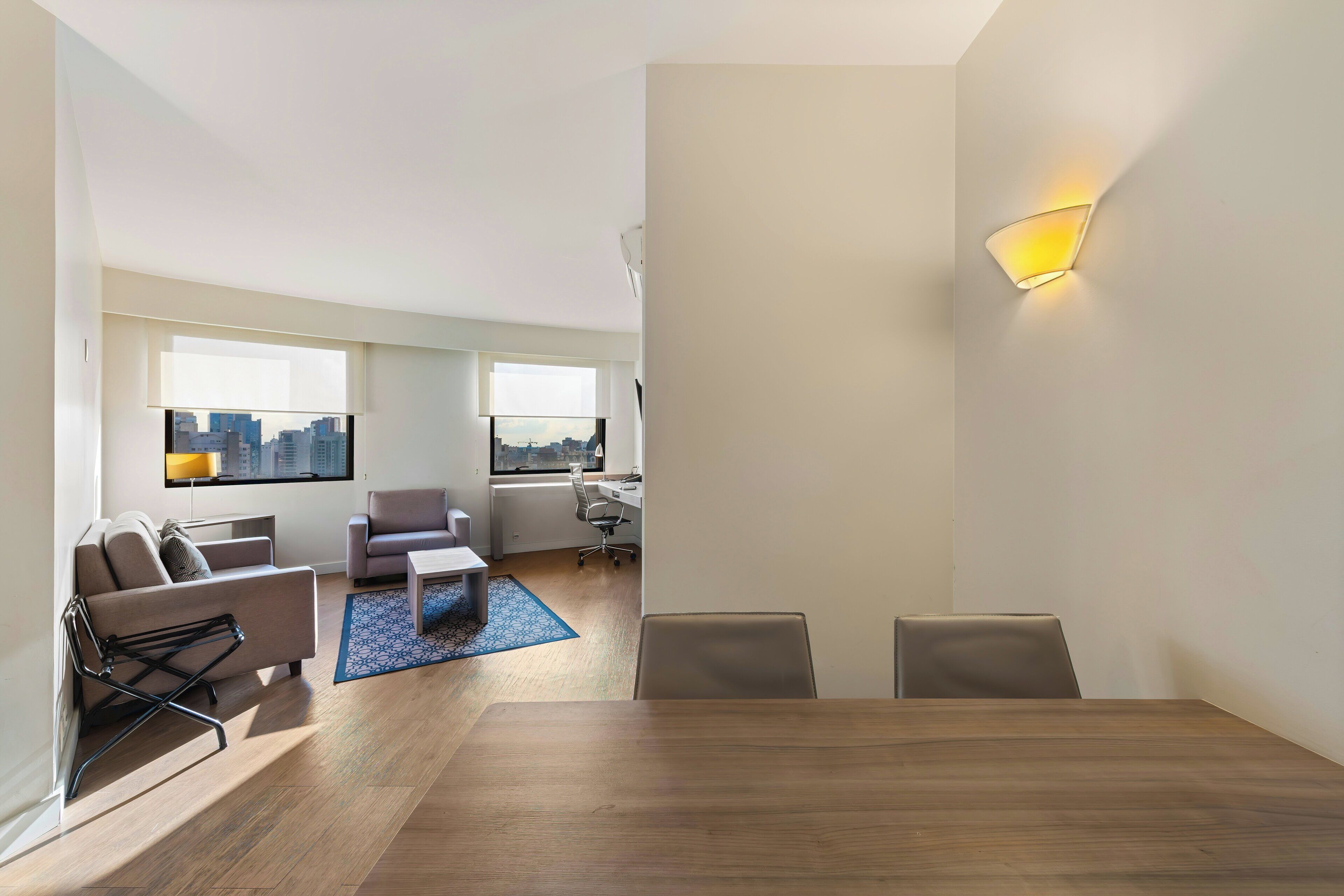 A modern living room with a dining area, a city view, and a workspace with a desk and chair.