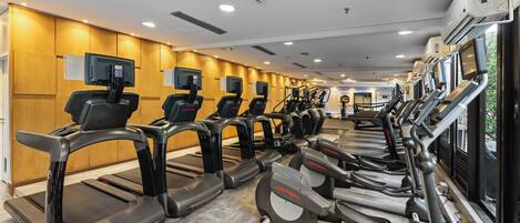 Une salle de sport équipée de plusieurs tapis de course et de vélos d’exercice, avec des murs recouverts de panneaux en bois et des unités de climatisation fixées au plafond.