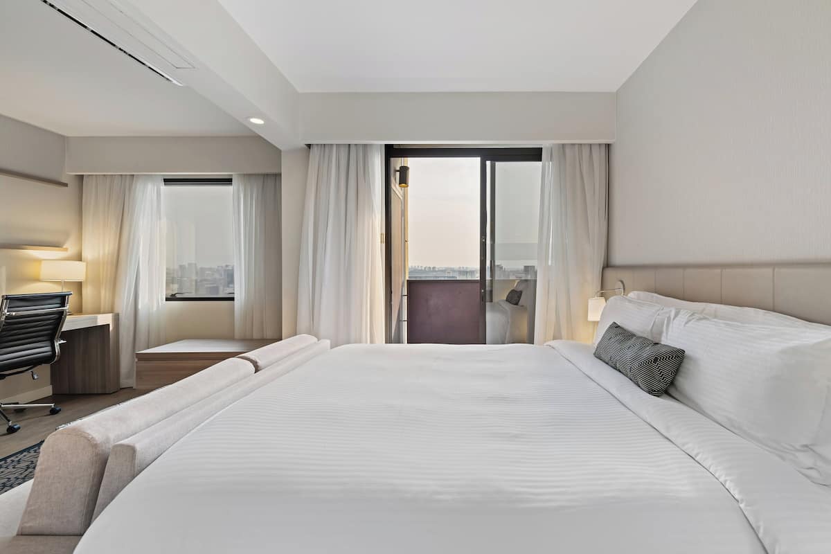 Une chambre d’hôtel moderne, dotée d’un grand lit, d’un bureau et offrant une vue sur la ville par la fenêtre.