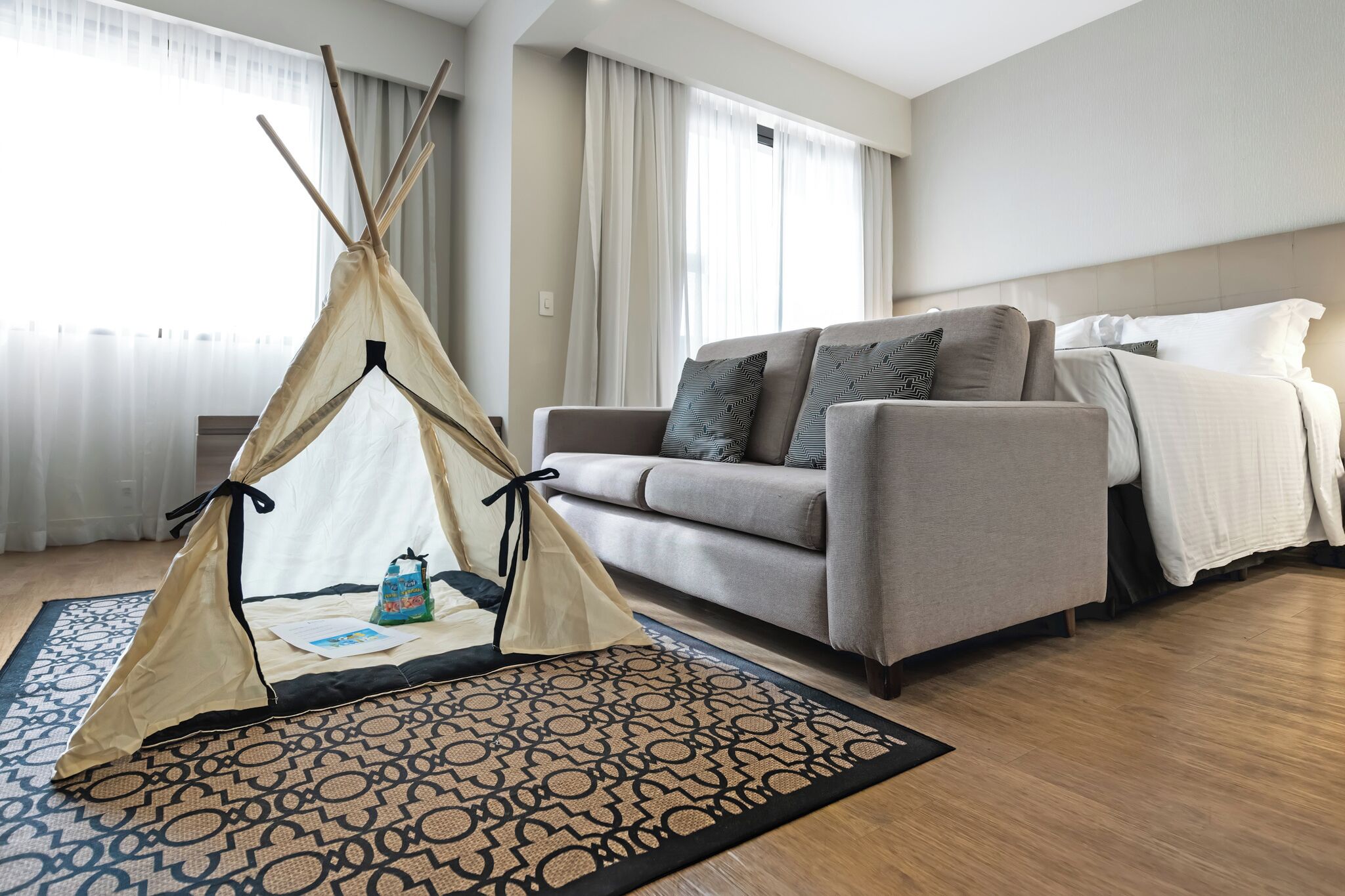 Moderni hotellihuone, jossa on sohva, sänky, kuvioitu matto ja teepeen muotoinen teltta.