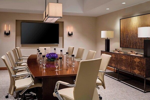 A conference room with a large table, chairs, a flat-screen TV, wall sconces, and a decorative panel.