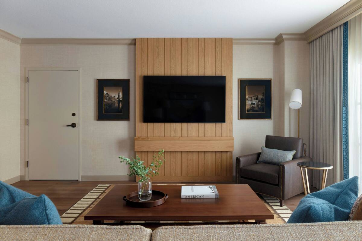 A modern living room with a flat-screen TV mounted on a wooden panel, a sofa, a coffee table with a book, and a side table.