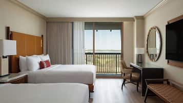 Habitación de hotel con dos camas, un escritorio, una silla, un televisor y un balcón con vistas.