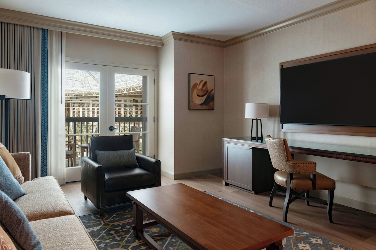 Une chambre d’hôtel équipée d’un canapé, d’une table basse, de deux fauteuils, d’un bureau, d’une télévision et d’un balcon avec vue.