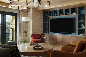 A modern living room with a large flat-screen TV, a round coffee table, a red armchair, and a bookshelf with books and decorative items.
