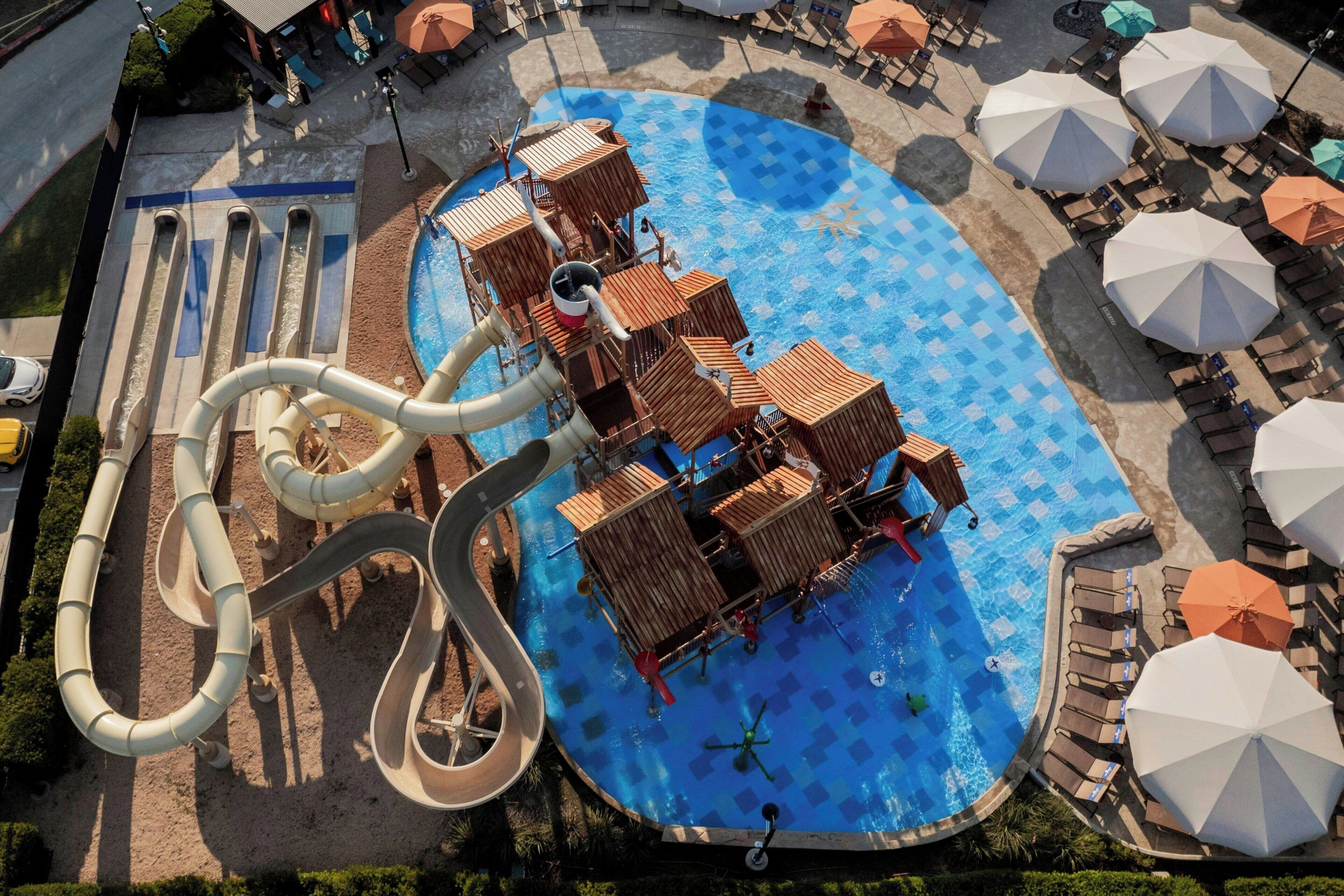 Parque acuático con una gran piscina, toboganes y juegos de madera.
