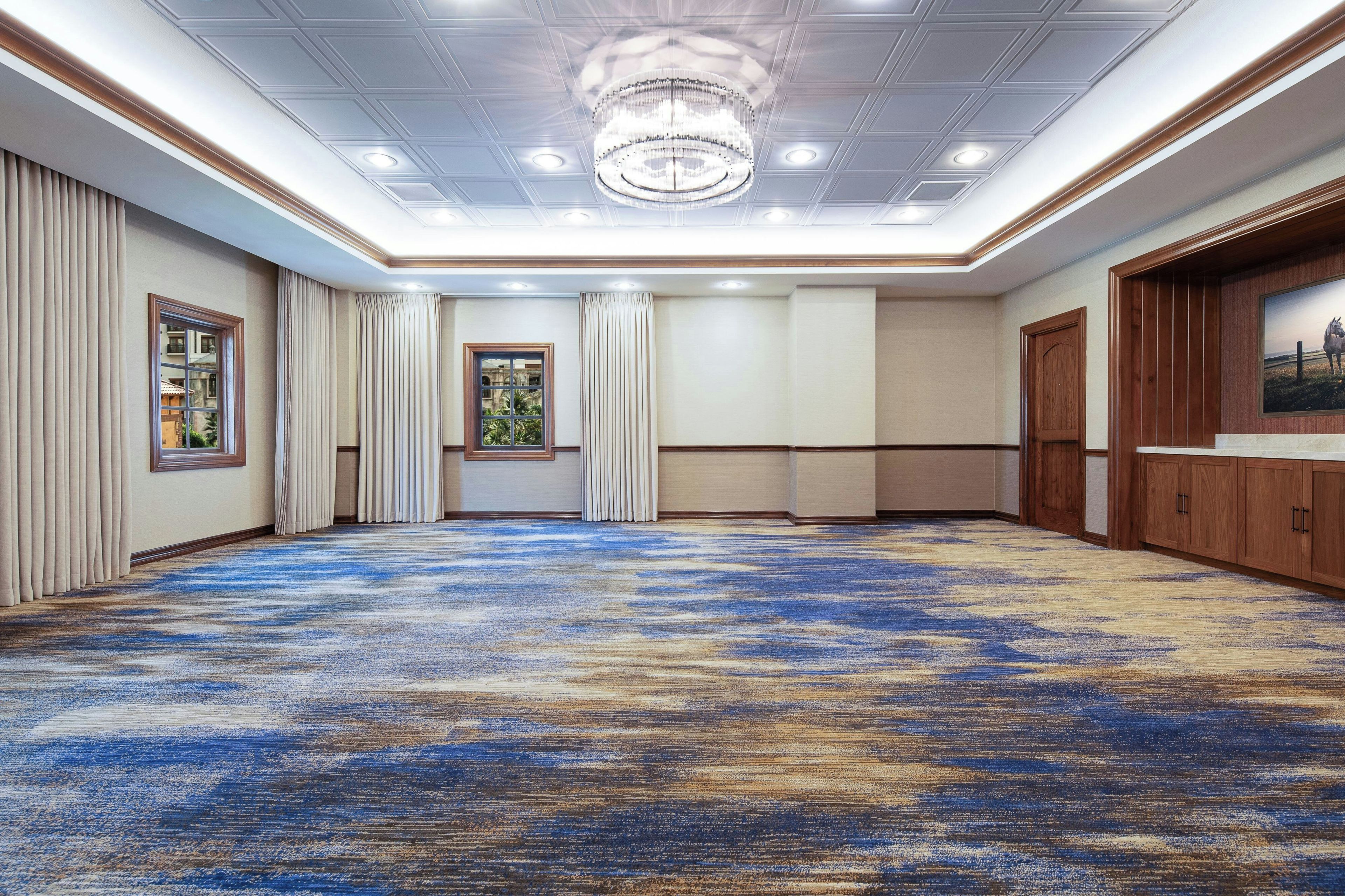 A spacious room with a patterned carpet, a chandelier, and a large window with curtains.