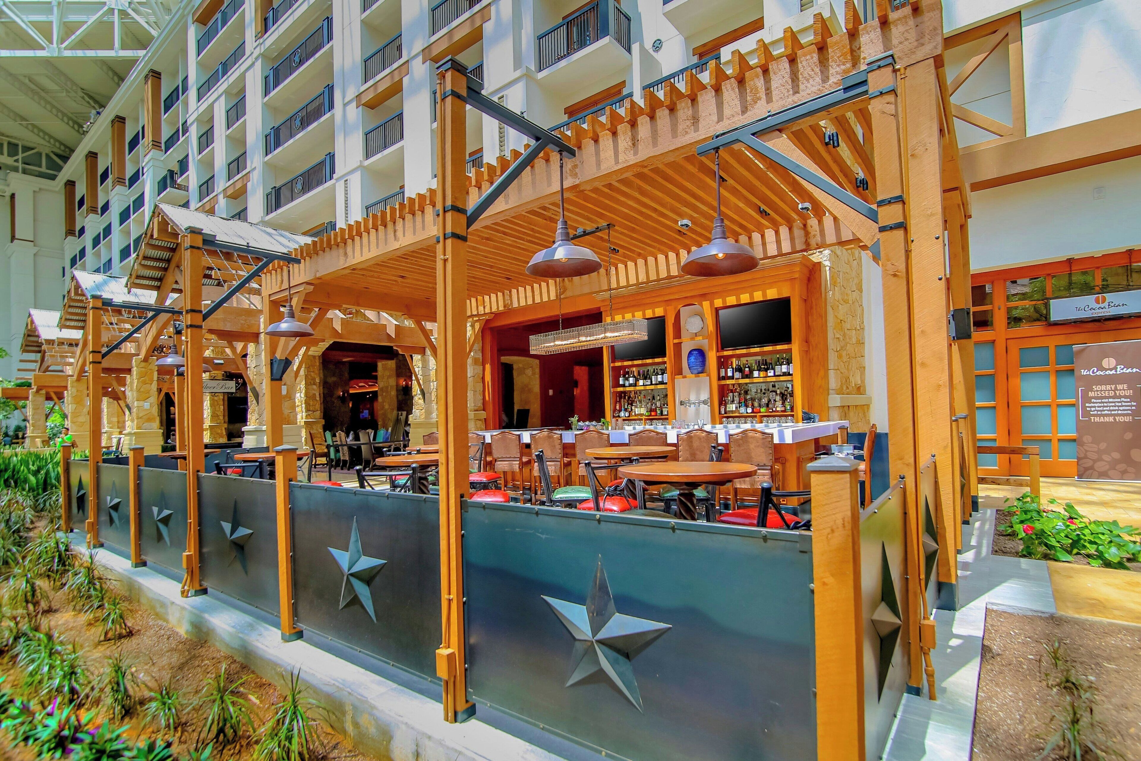 An indoor atrium with a bar area, multiple seating arrangements, and a view of the surrounding building.