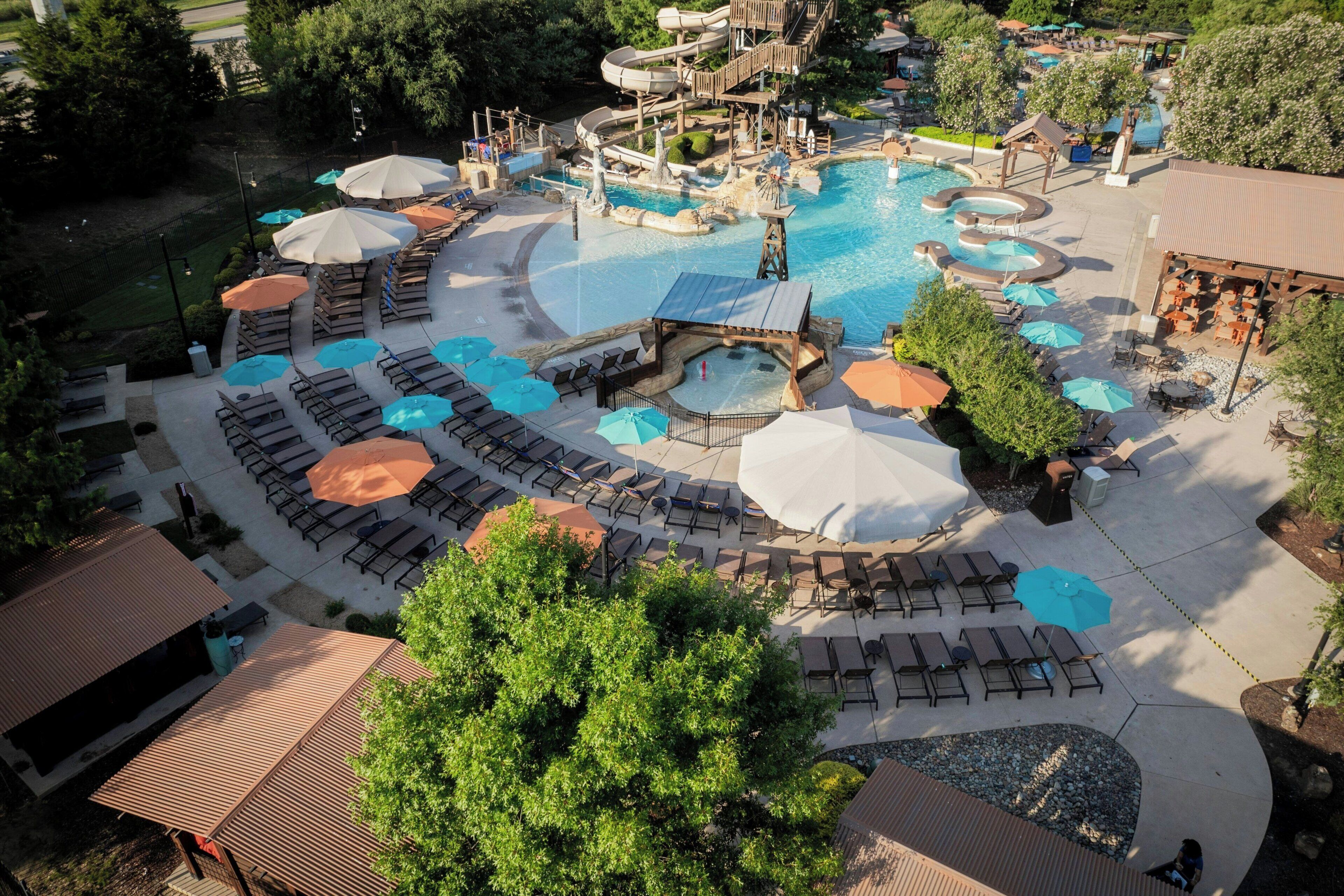 Un complejo turístico con piscina central, toboganes acuáticos y zonas de estar al aire libre con sombrillas.