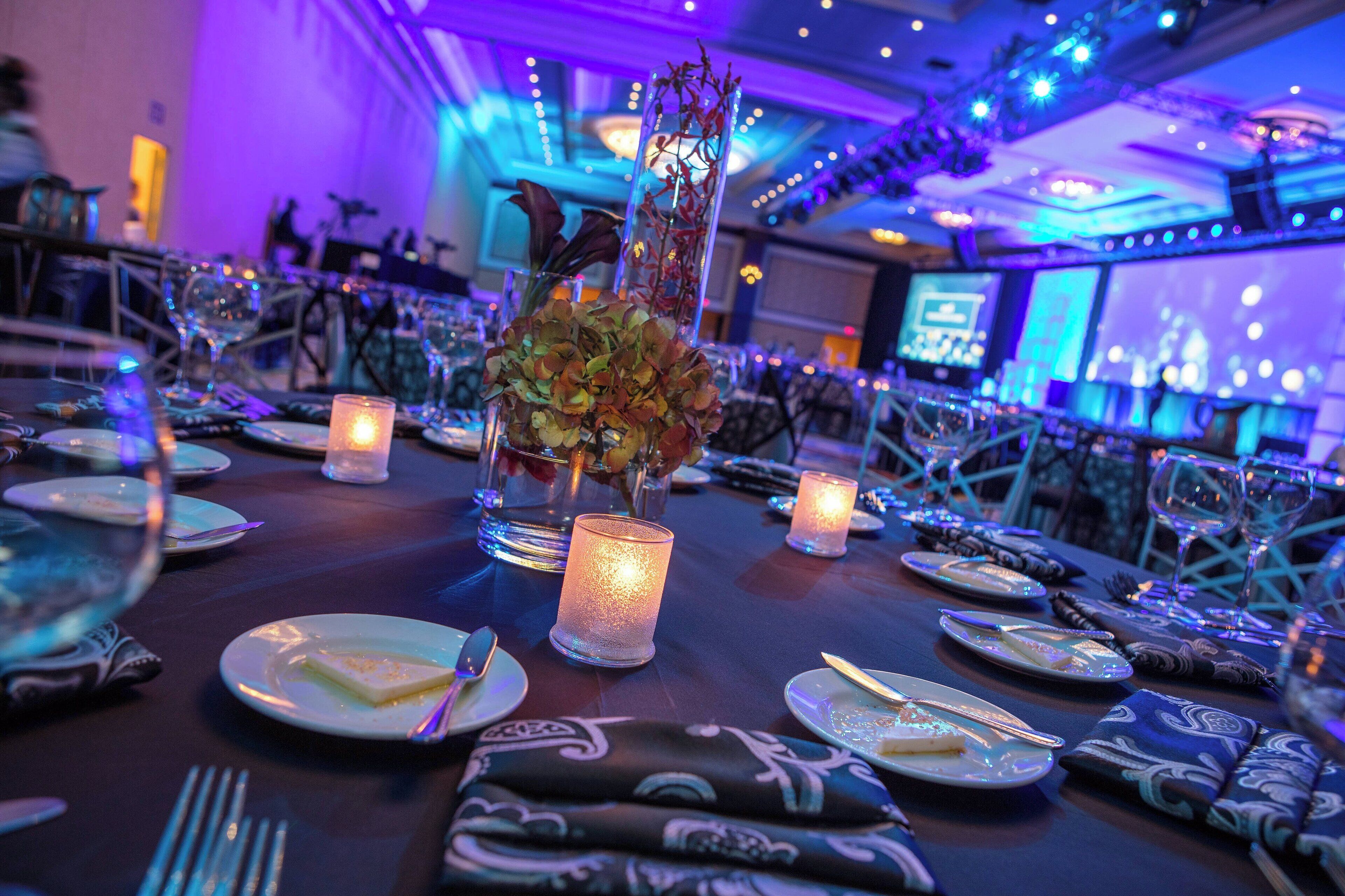 A dining table set with plates, cutlery, and candles, with a decorative centerpiece.