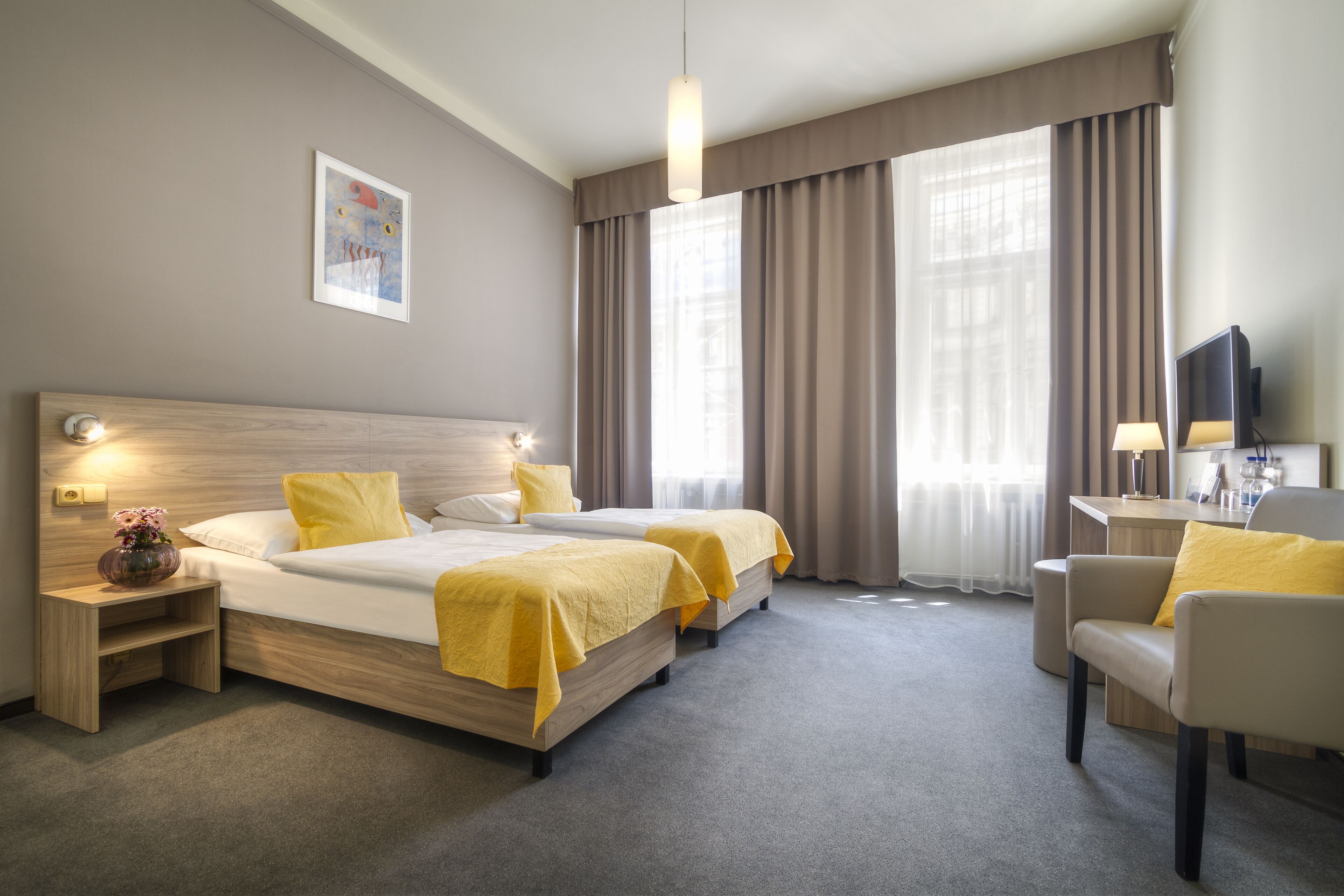 A hotel room with two beds, a desk, a chair, and a TV.