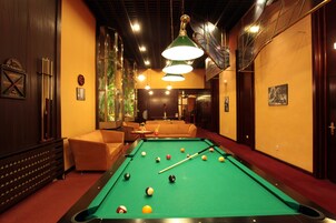 Een pooltafel met ballen, een bank en een biljarthouder in een kamer met houten wanden en een rood tapijt.