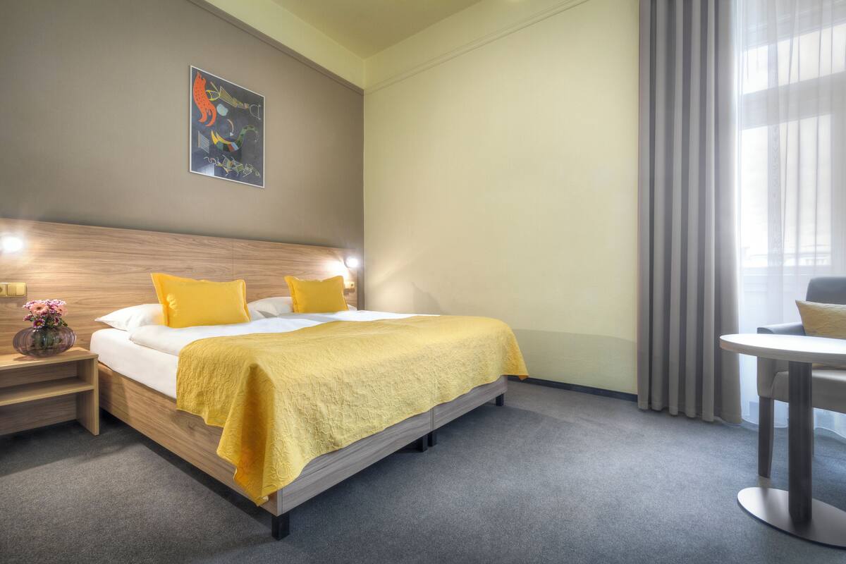 Una habitación de hotel con una cama, una mesita de noche y una pequeña mesa con una silla.