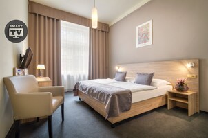 Quarto de hotel moderno com cama, cadeira, escrivaninha e televisão.