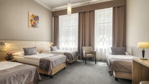 A hotel room with three beds, a desk, a chair, and a large window with curtains. - Atlantic Hotel (Prague)