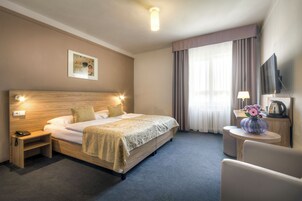 Quarto de hotel com uma cama grande, luminárias de cabeceira, uma TV de tela plana, uma mesinha com um vaso e um quadro na parede.