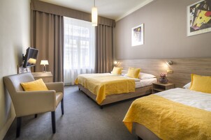 Quarto de hotel com duas camas, uma cadeira, uma escrivaninha e uma televisão.