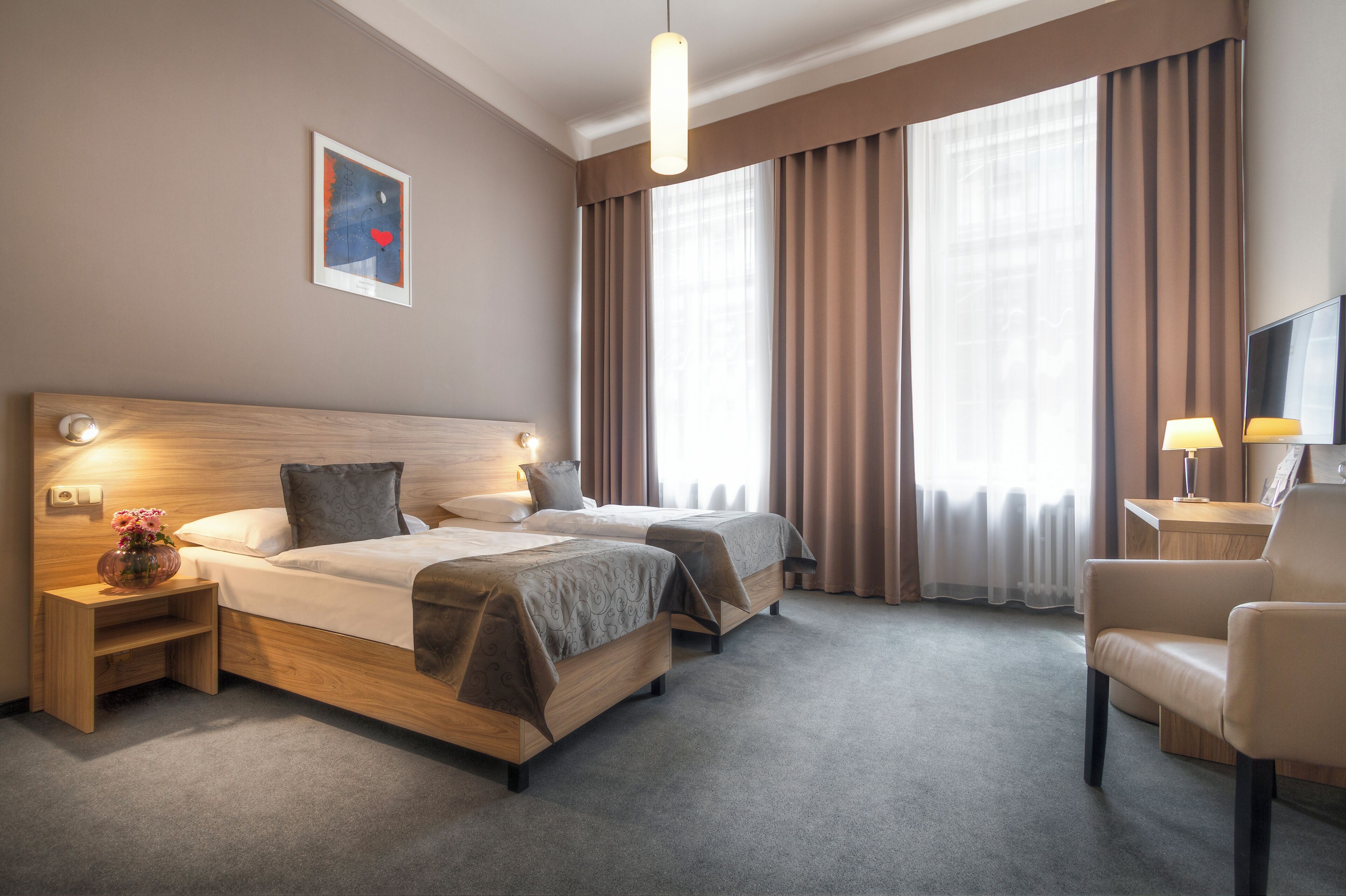 A hotel room with two beds, a desk, a chair, a TV, and a window with curtains.