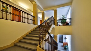 A grand staircase with ornate iron railings and a carpeted floor, leading to a landing with a potted plant. - Atlantic Hotel (Prague)