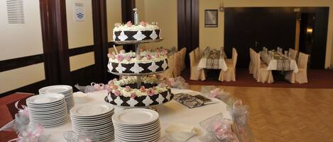 Un pastel de tres niveles con cobertura blanca y negra y flores rosadas sobre una mesa con platos y servilletas blancos.