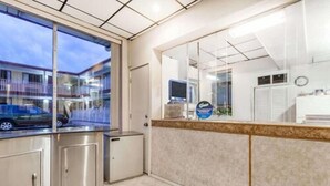 A reception area with a glass partition, a reception desk, a computer, and a clock on the wall. - Atlantic Motor Inn (Atlantic City)