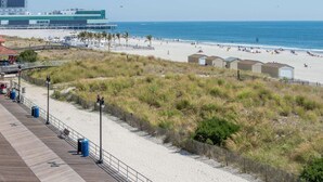 A beach with a wooden boardwalk, beach huts, and a distant view of a building. - Atlantic Motor Inn (Atlantic City)