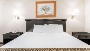 A hotel room with a large bed, two bedside tables, a nightstand, a framed artwork above the bed, and wall-mounted lamps. - Atlantic Motor Inn (Atlantic City)