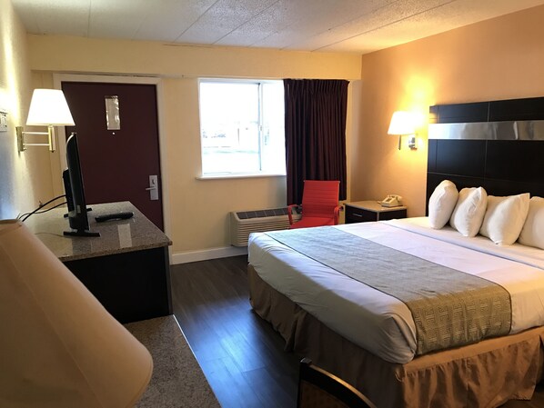 A hotel room with a bed, bedside lamps, a desk with a computer, a chair, and a window with curtains.
