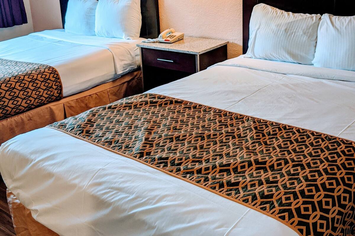 A hotel room with two beds, a nightstand with a phone, and wall-mounted lamps.