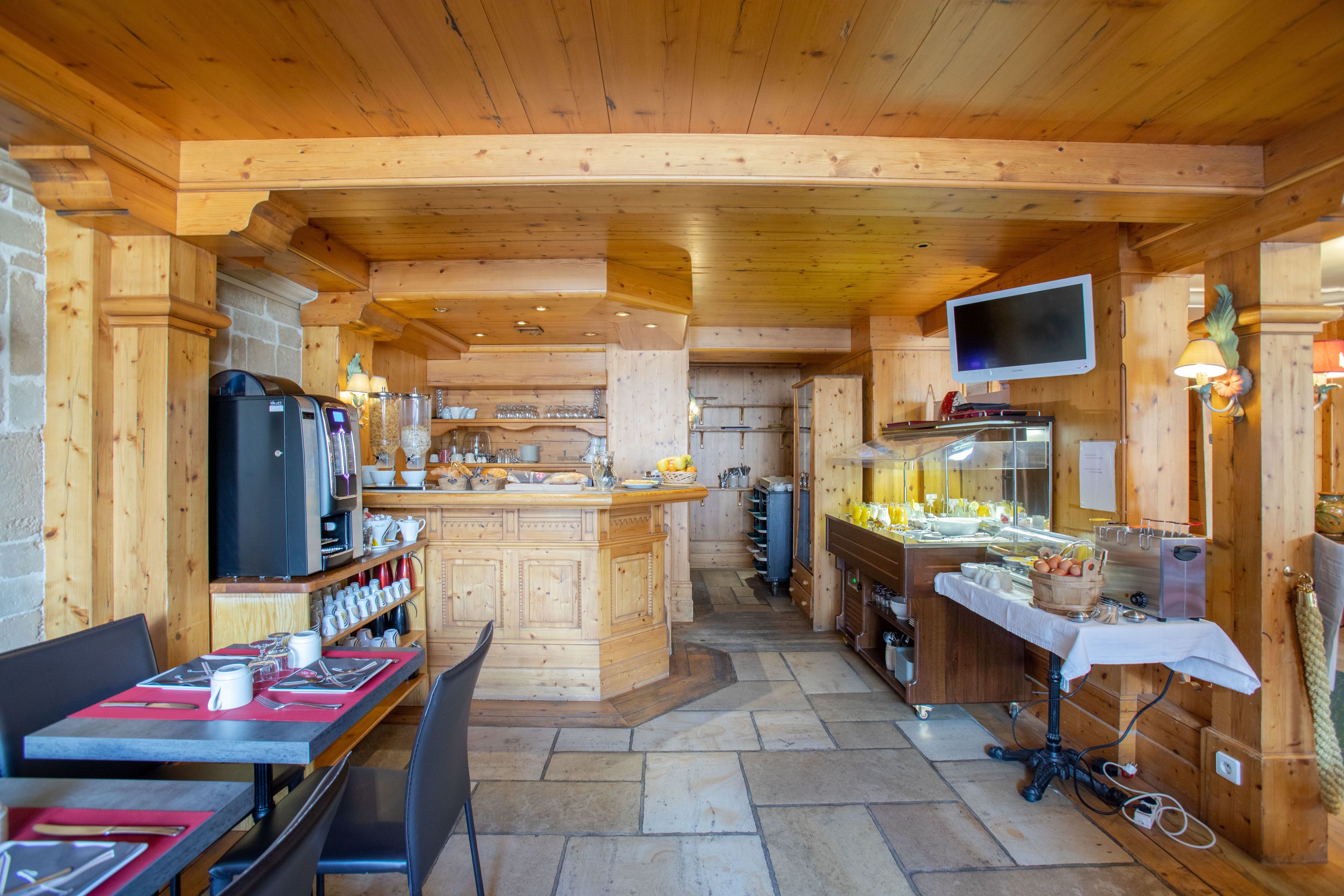 Un interior de madera con una isla central, mesas con sillas, una zona de cocina y un televisor montado en la pared.