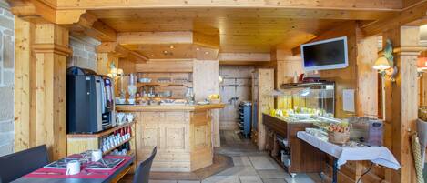 Un interior de madera con una isla central, mesas con sillas, una zona de cocina y un televisor montado en la pared.