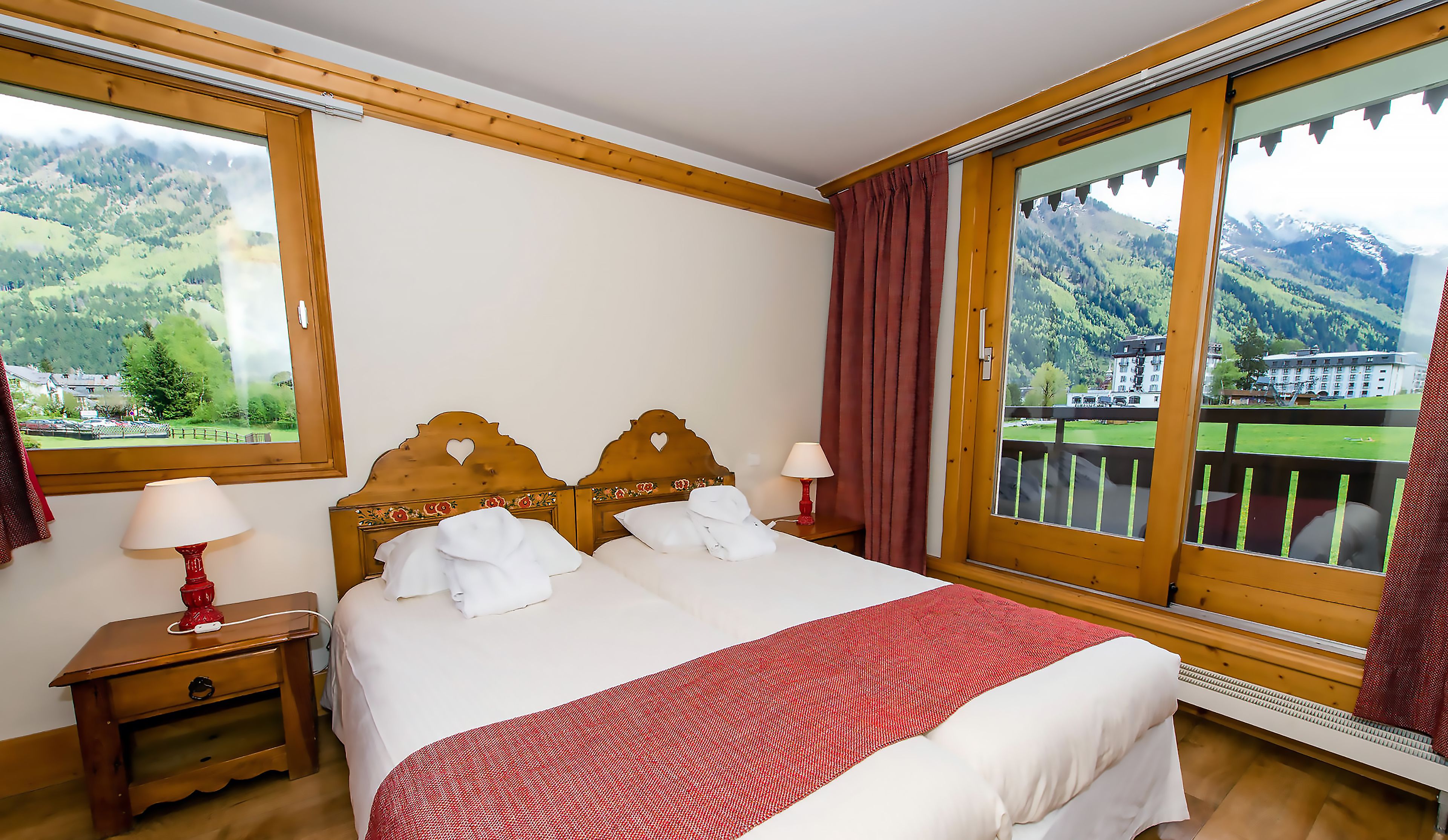 Une chambre d’hôtel comprenant un lit, deux tables de chevet, une fenêtre donnant sur la montagne et un balcon avec une balustrade.