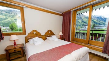Une chambre d’hôtel comprenant un lit, deux tables de chevet, une fenêtre donnant sur la montagne et un balcon avec une balustrade.
