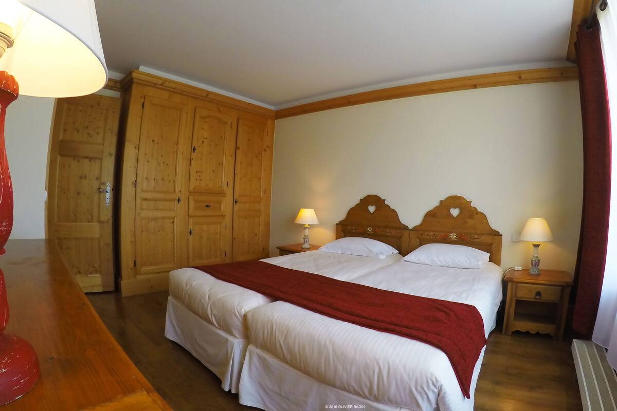 En dobbeltseng med træsengestolpe, to sengeborde med lamper, et træskab og et rødt plaide.'