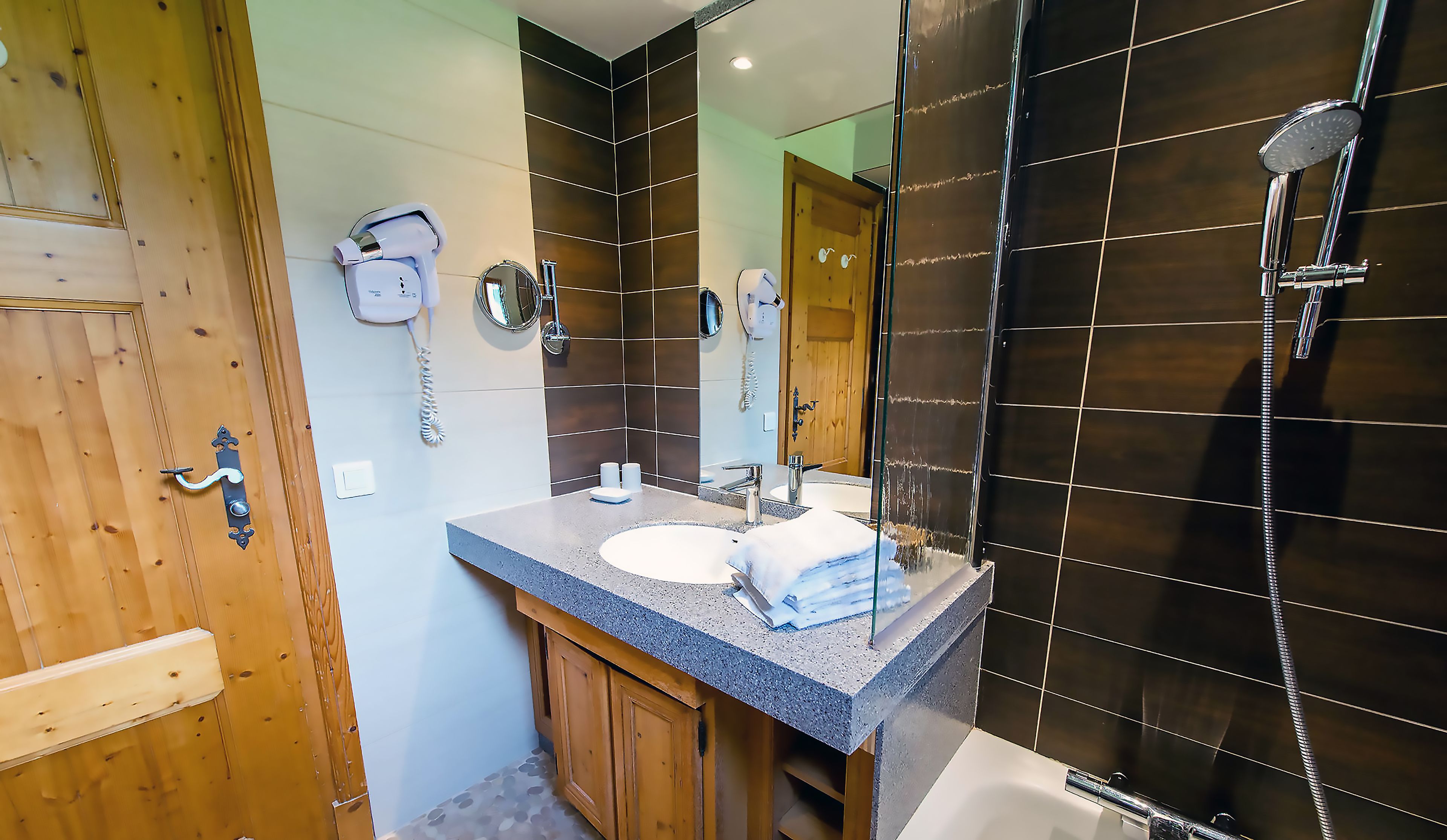 A bathroom with a wooden door, a sink with a mirror, a hairdryer, and a shower.