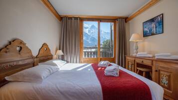 A hotel room with a bed, a wooden headboard, a nightstand, a lamp, a painting, and a view of mountains through a large window.