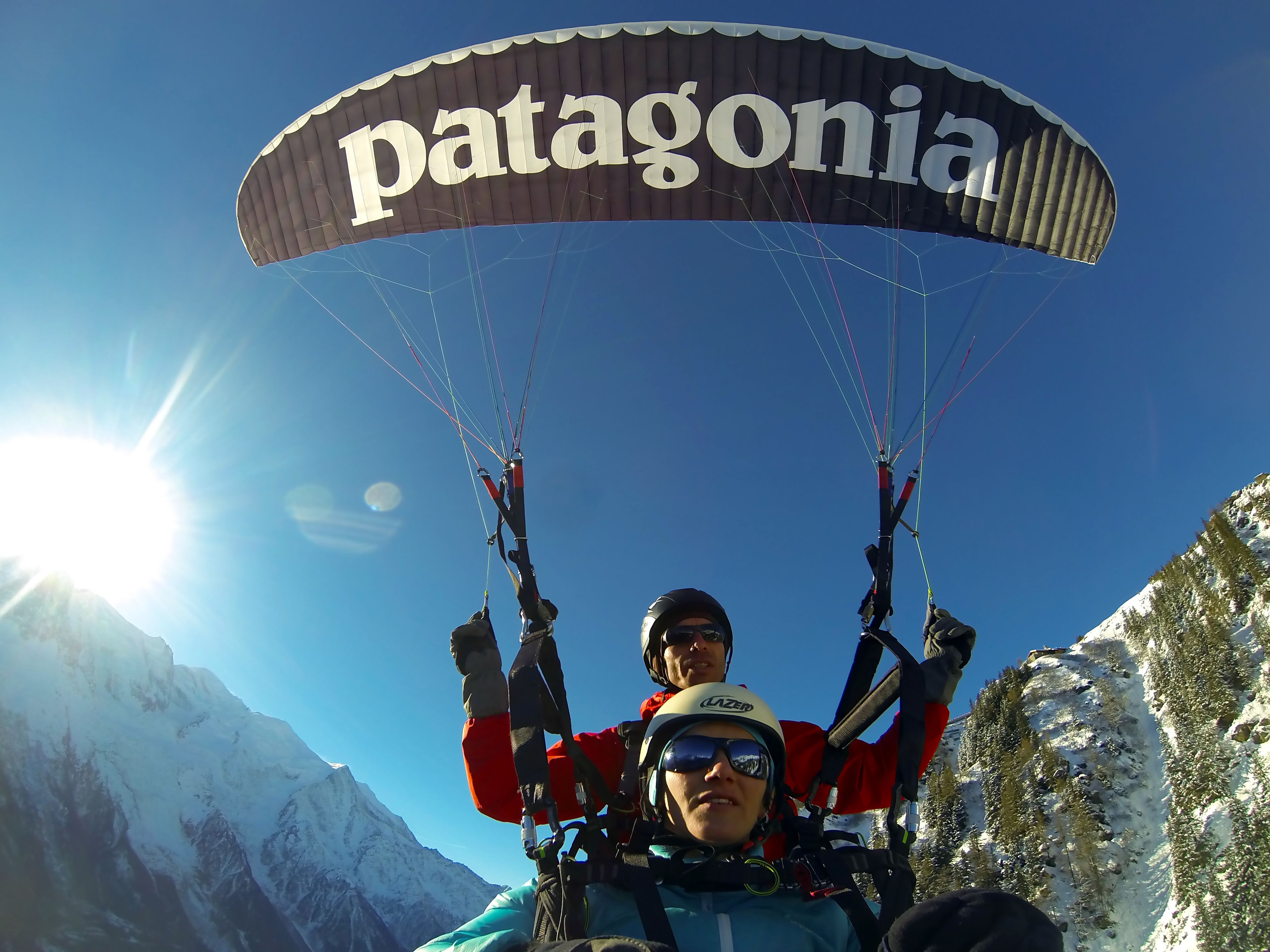 A person paragliding with a parachute labeled "Patagonia" against a mountainous backdrop.