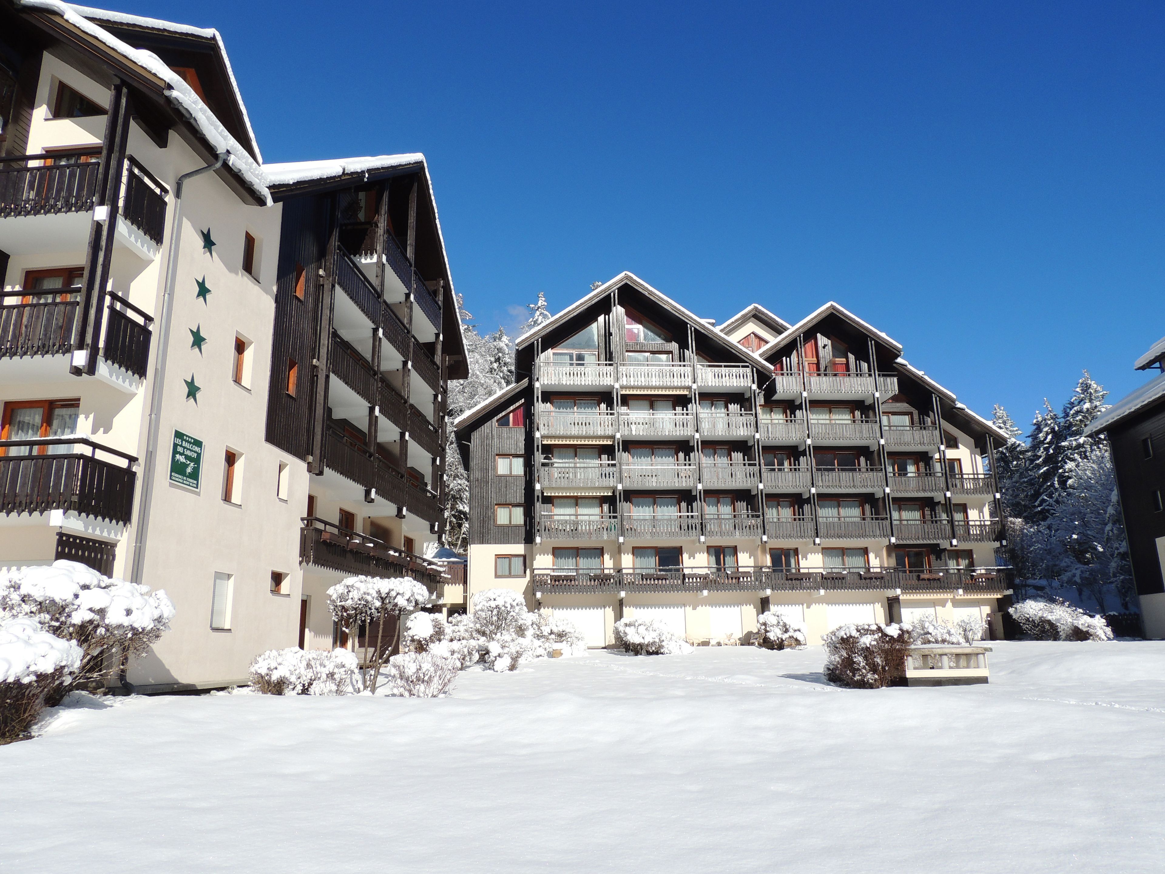 Ett hotell med flera våningar, balkonger, ett snötäckt landskap och en klarblå himmel.
