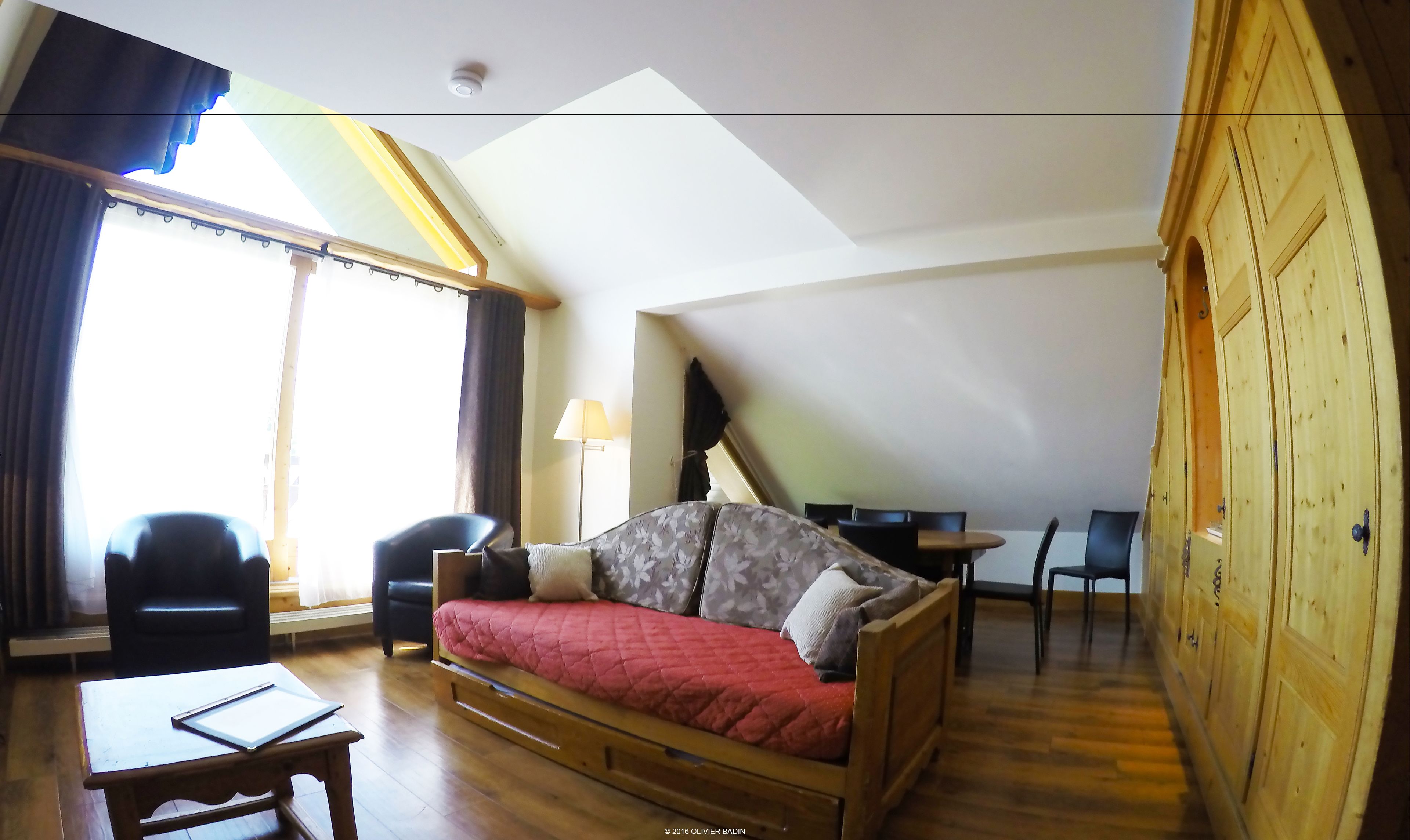 Um quarto aconchegante com um sofá de madeira, uma mesinha e uma escrivaninha com cadeiras.