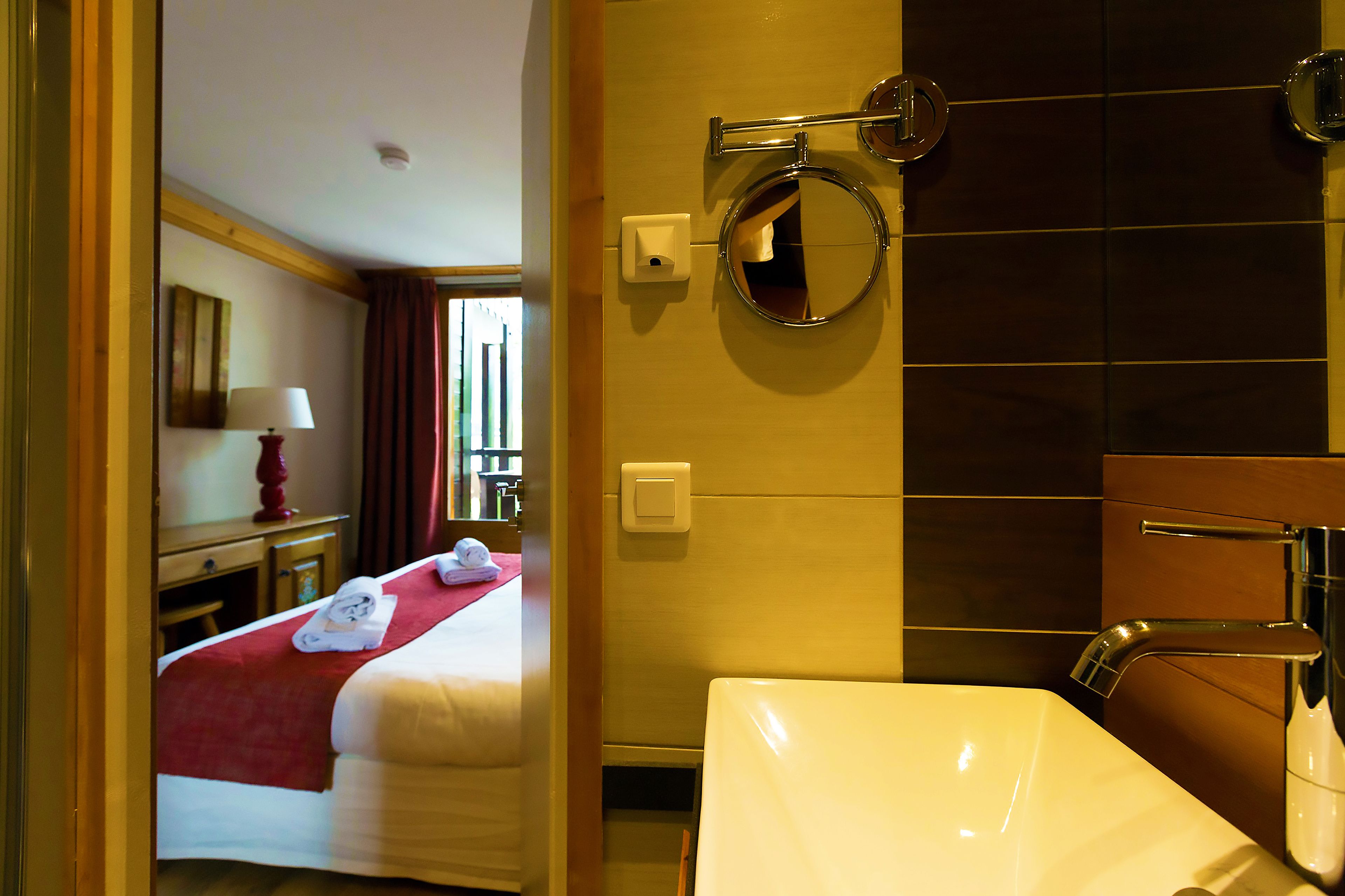 Ein Hotelzimmer mit Bett, einem Badezimmer mit Waschbecken und Spiegel sowie einem Fenster mit Vorhängen.
