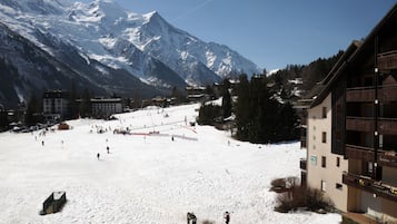 A snow-covered ski slope with buildings and mountains in the background.