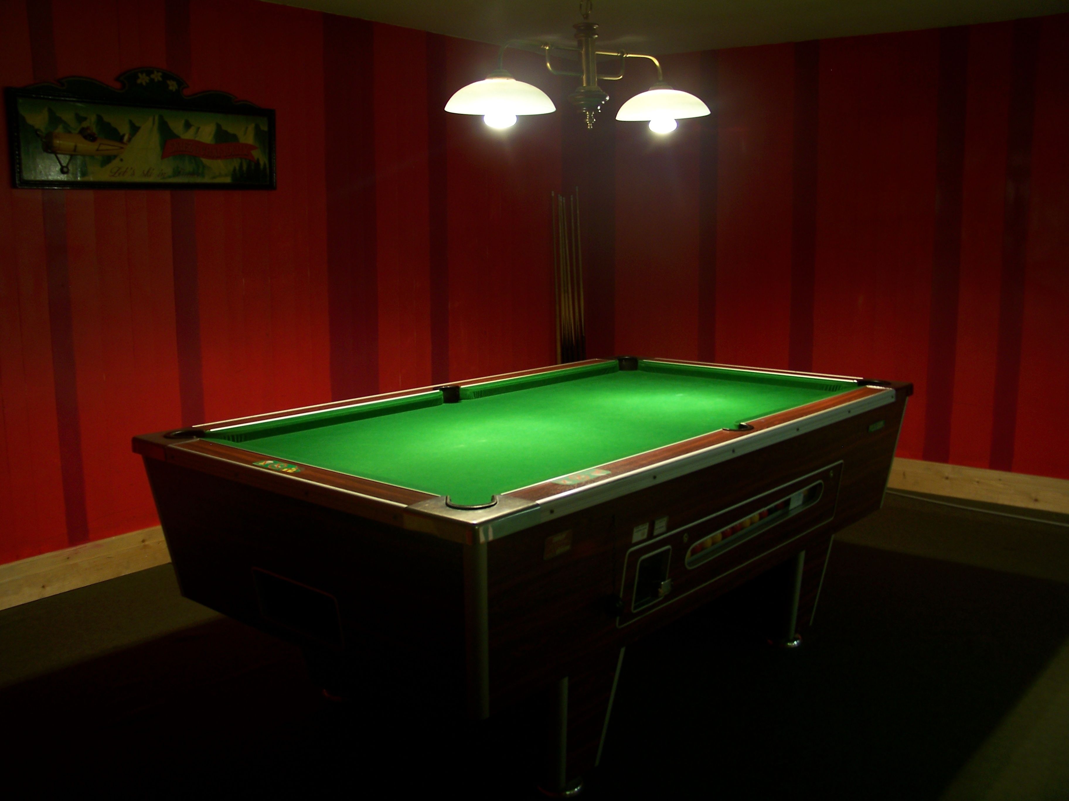A pool table in a room with red walls and a framed picture on the wall.