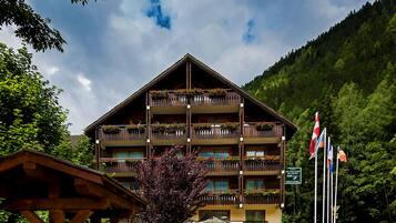 Et hotel med flere etager, altaner pyntet med blomster, et skilt der angiver en beliggenhed i Savoie, samt flag på en flagstang.